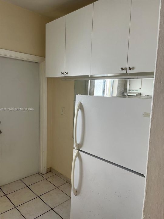 White flat-panel upper cabinetry, mirrored backsplash, and ceramic tile flooring