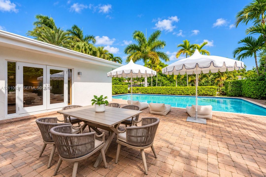 Backyard patio featuring paver hardscaping, a swimming pool, and mature palm trees enclosed by manicured hedges
