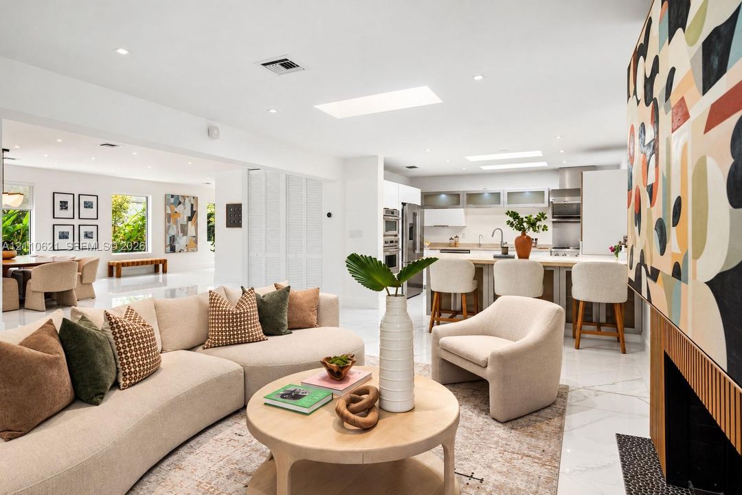 Open-concept living space featuring high ceilings with integrated skylights, polished stone-finish flooring, and a fireplace with wood-slat detailing