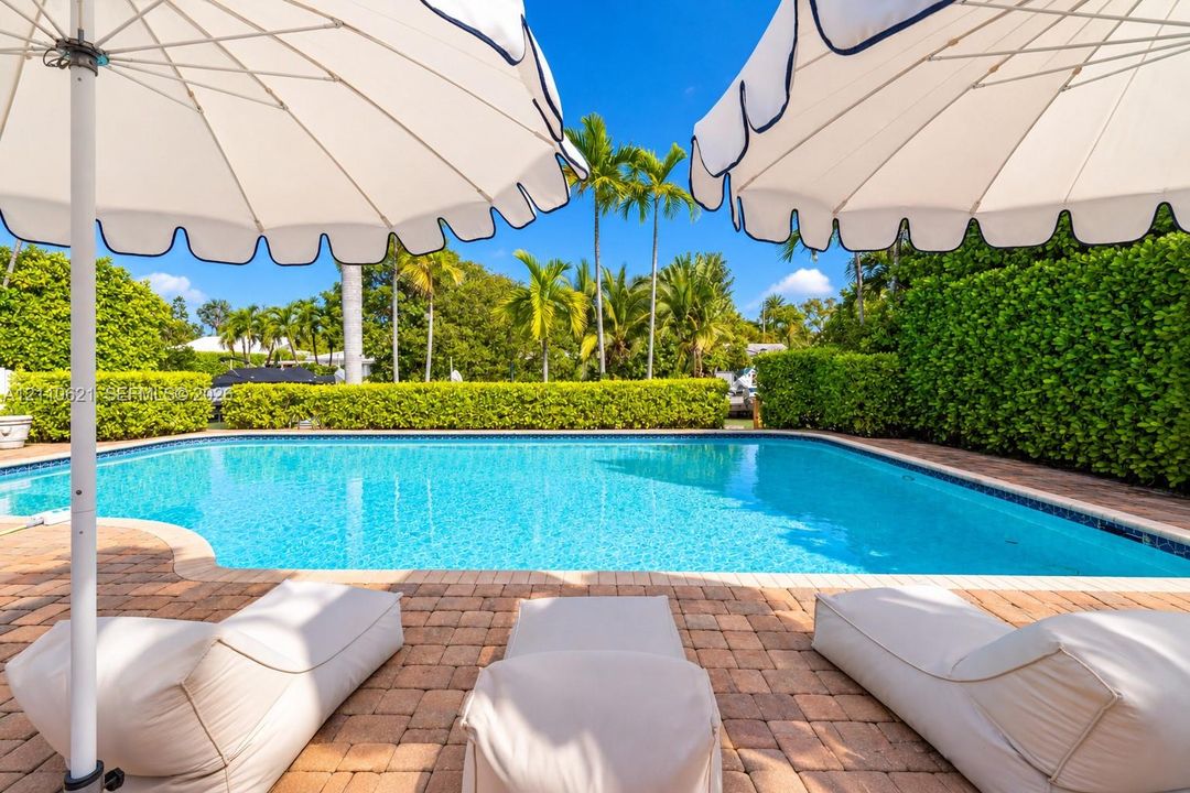 In-ground swimming pool featuring a brick paver deck, perimeter privacy hedges, and mature palm trees