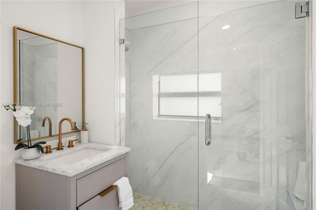 Modern vanity with stone-look countertop, brass-finish faucet, and framed mirror