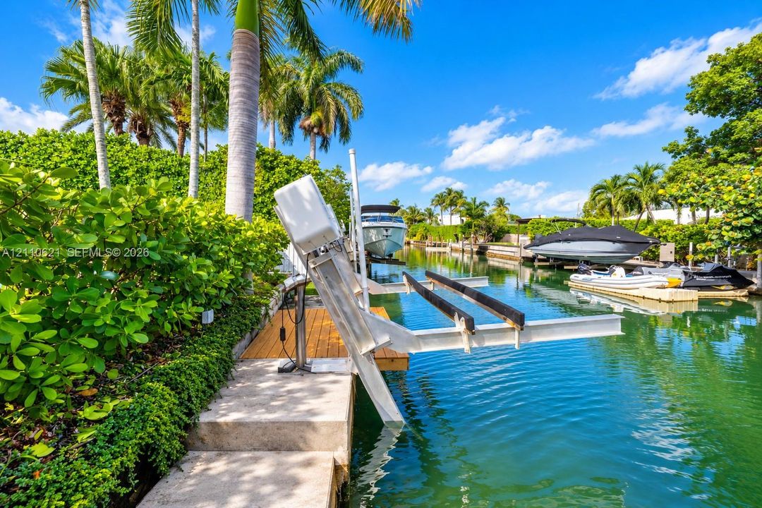 Waterfront property featuring a canal-side boat lift, wood-plank decking, concrete bulkhead, and mature tropical landscaping
