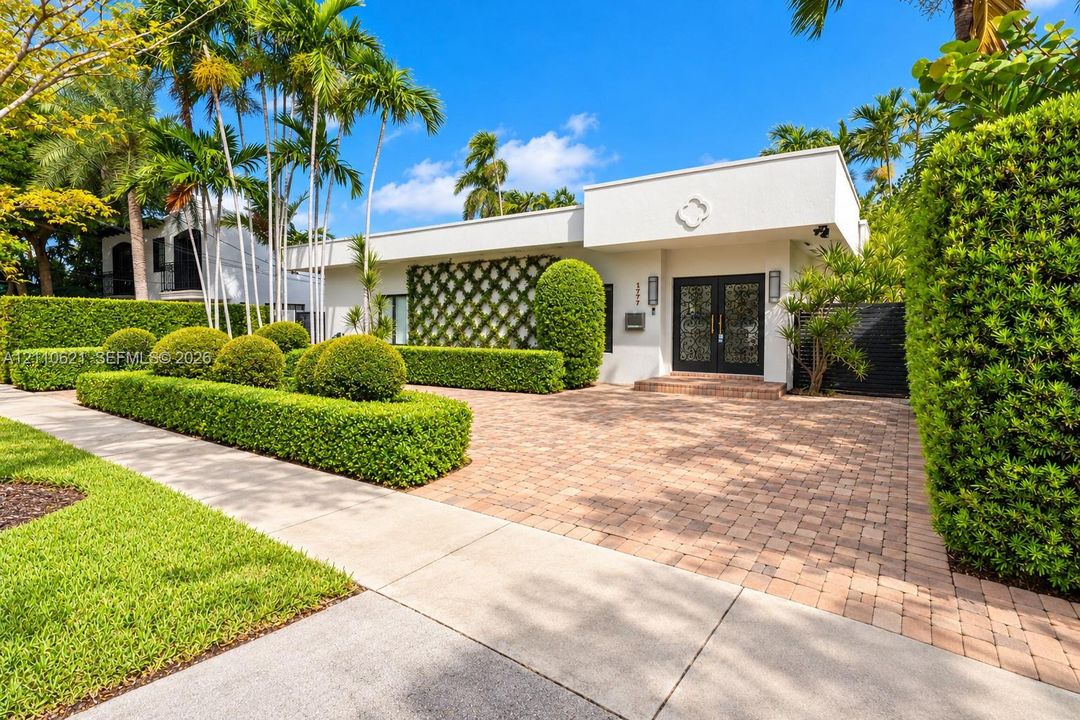 Modern stucco exterior featuring a patterned wall trellis, paver driveway, double glass-paneled entry doors, and professional landscaping