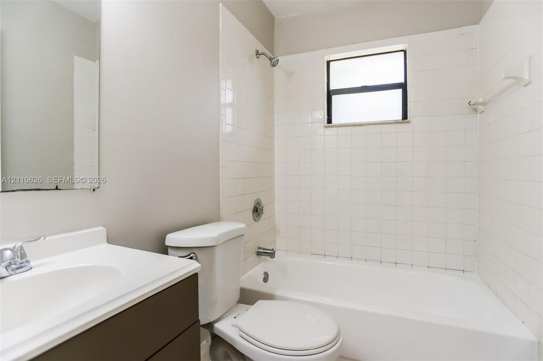 Bathroom featuring a white bathtub, white wall tiling, single-basin vanity with a white countertop, and a built-in window