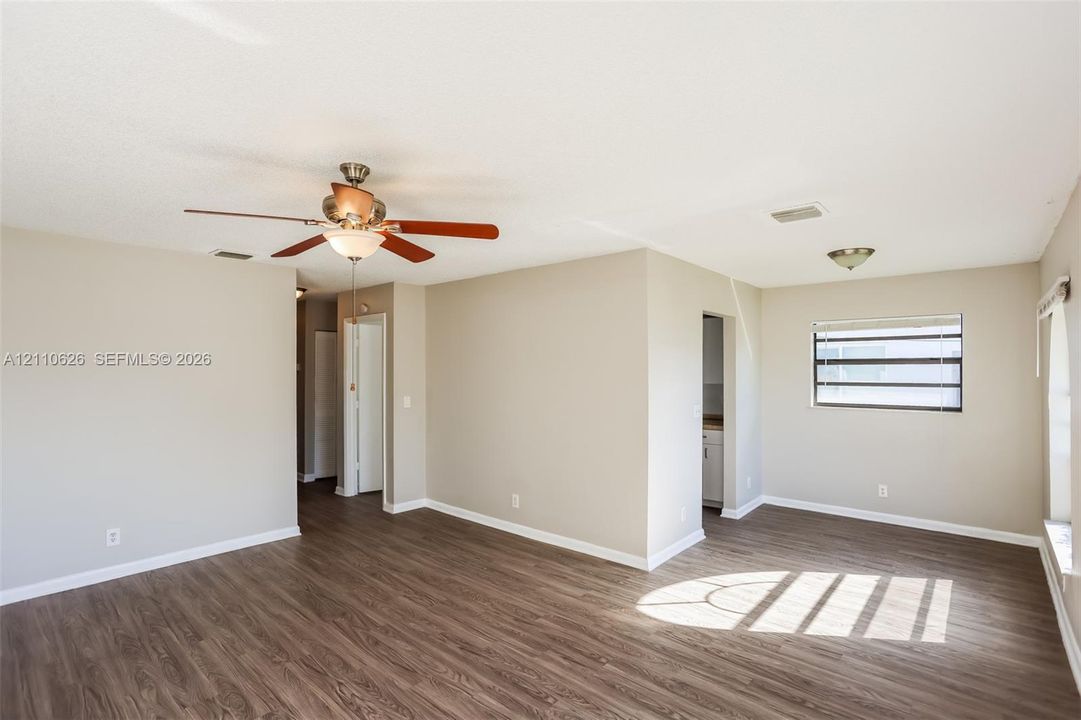 Neutral-toned interior space featuring wood-finish flooring, a ceiling fan with integrated lighting, and horizontal slatted windows