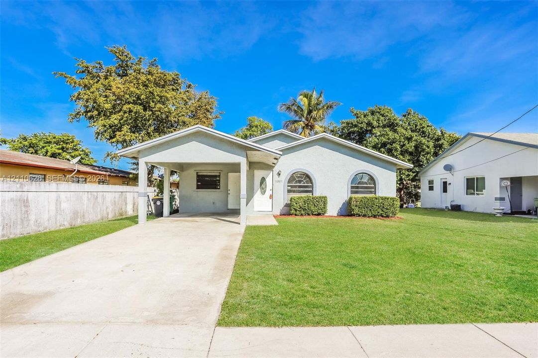 Single-story exterior featuring a light-toned stucco facade, arched windows, covered carport, and a manicured front lawn