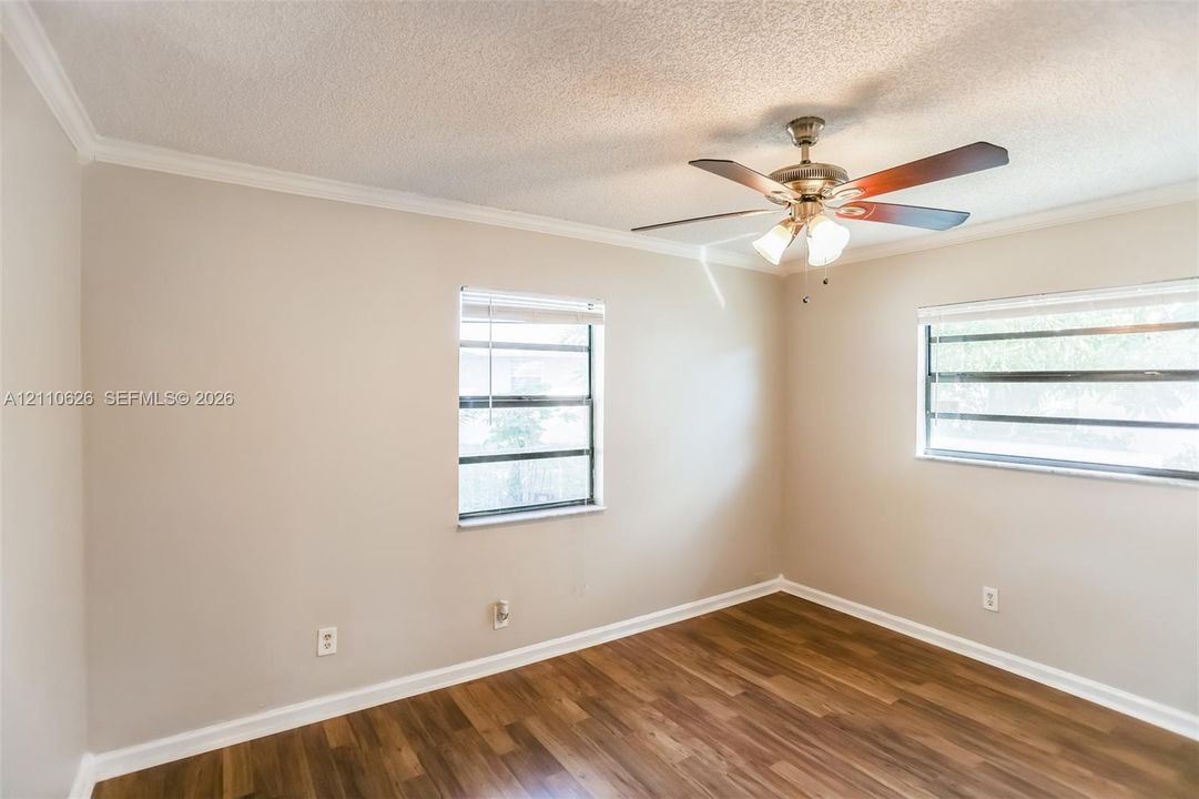 Room featuring wood-finish flooring, dual windows with blinds, and a ceiling-mounted fan with integrated lighting