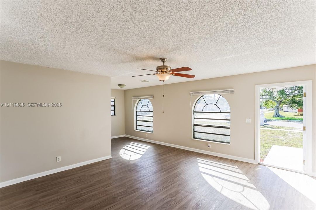 Interior room featuring wood-finish flooring, two arched windows with grid detailing, and a central ceiling fan with integrated lighting