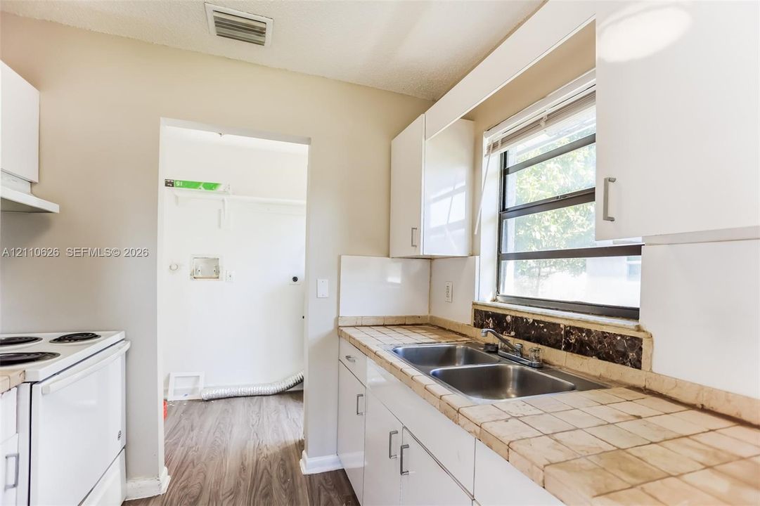 Kitchen featuring white cabinetry, tiled countertops, double-basin stainless steel sink, and wood-finish flooring