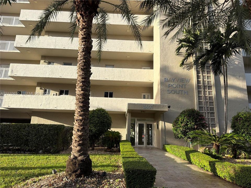 Multi-story stucco exterior featuring private recessed balconies, a covered entryway, and mature palm tree landscaping