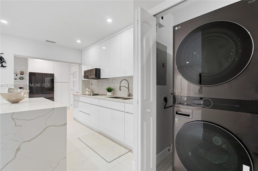 Kitchen featuring high-gloss cabinetry, stone-finish countertops, waterfall island, and built-in stacked laundry unit