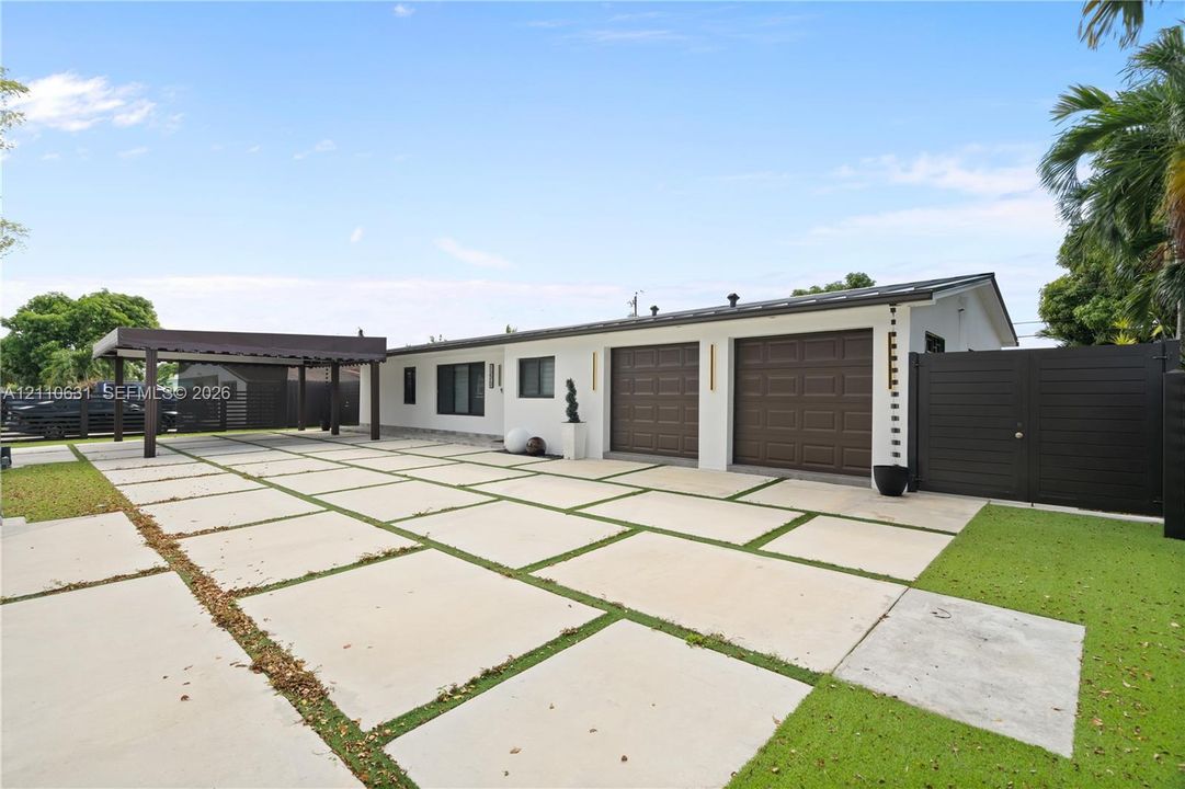 Exterior featuring a double-bay garage, a detached covered carport, wide-format concrete paver driveway with integrated turf, and perimeter privacy fencing