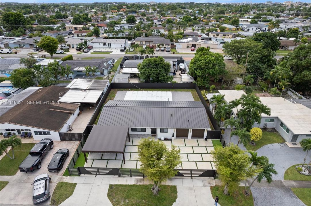 Aerial perspective featuring a metal roof, attached carport, multi-car garage, perimeter fencing, and paver driveway