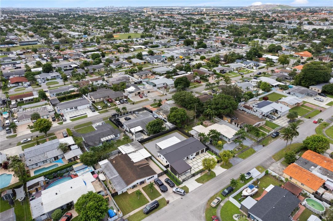 Aerial view featuring a residential property with a metal roof, a paved geometric driveway, a detached carport, and a fenced perimeter