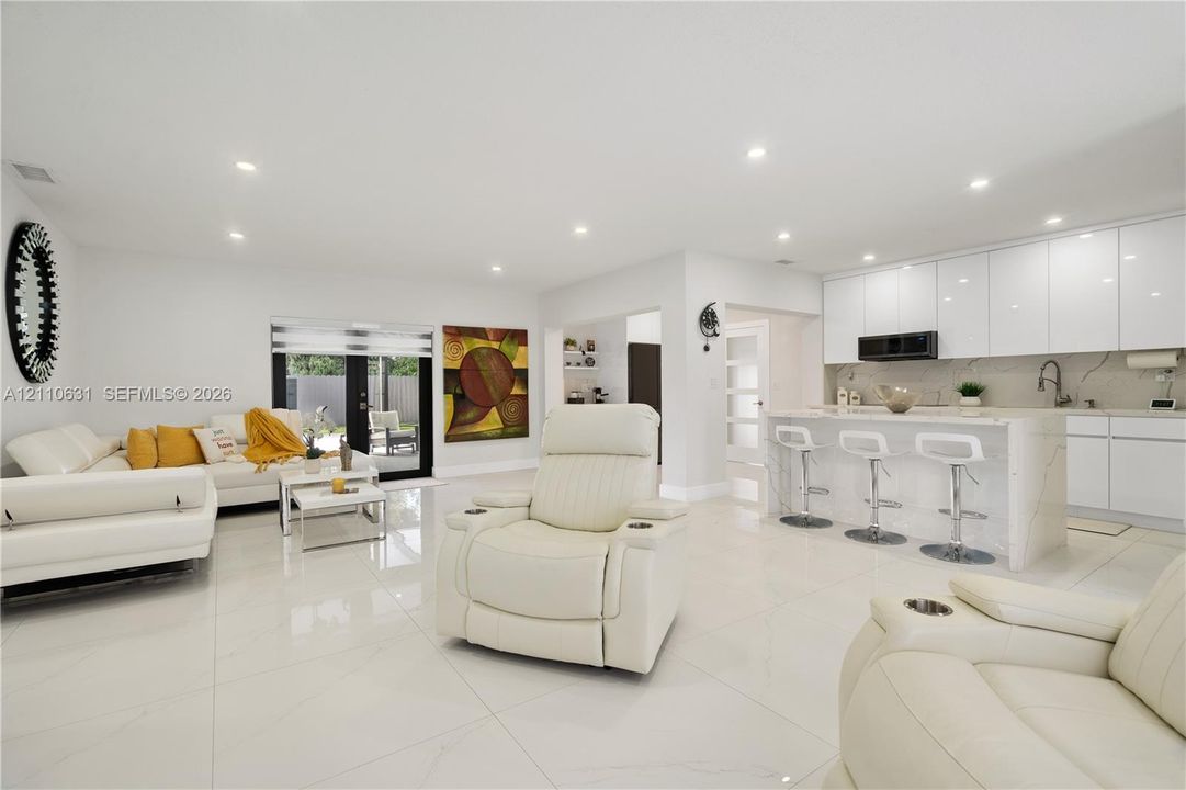 Open-concept kitchen featuring high-gloss cabinetry, stone-finish countertops, waterfall-edge island, large-format tile flooring, and recessed lighting
