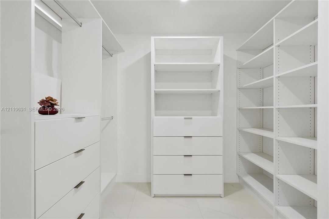 Custom walk-in closet featuring white built-in cabinetry, integrated shelving units, deep-drawers with modern pulls, and hanging rods