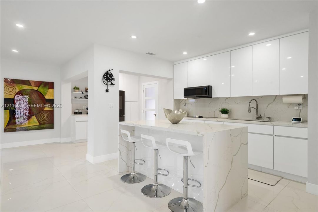 Kitchen featuring flat-panel white cabinetry, stone-patterned countertops, waterfall-edge island, built-in microwave, and recessed ceiling lighting