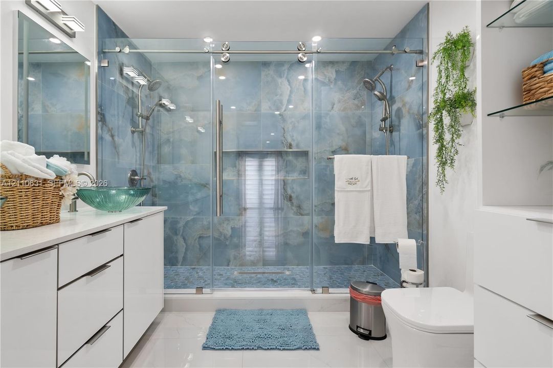 Walk-in shower featuring large-format blue stone-finish wall tile, frameless glass enclosure with sliding hardware, and built-in recessed niche