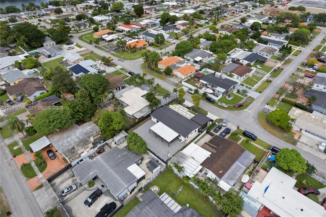 Aerial view featuring a single-story residence with a multi-section roofline, an attached covered carport, a paved driveway, and mature perimeter landscaping