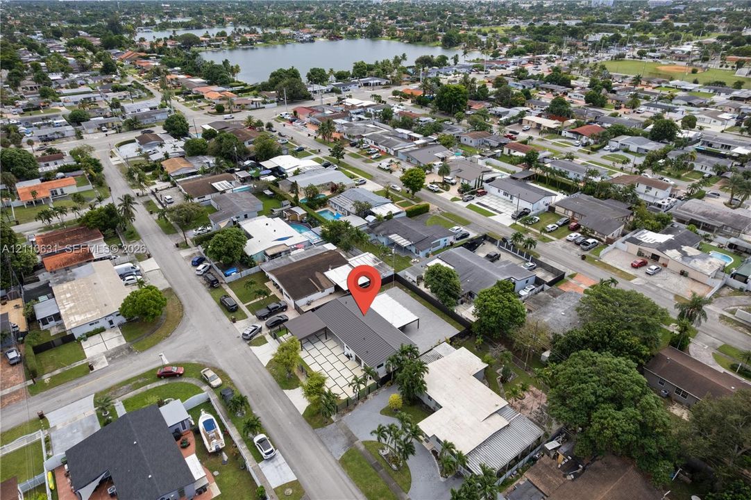 Aerial perspective of a property featuring a dark-toned gable roof, a concrete paver driveway with grass inlay, a metal-framed carport, and mature perimeter trees