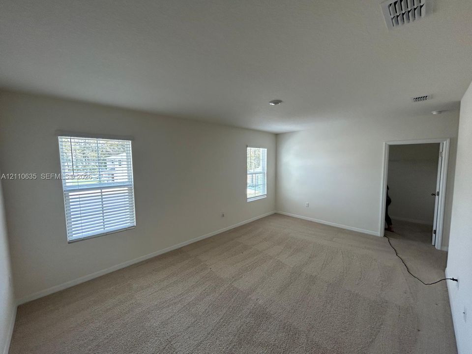 Neutral-toned interior space featuring wall-to-wall carpeting, dual windows with fitted blinds, and a walk-in storage area