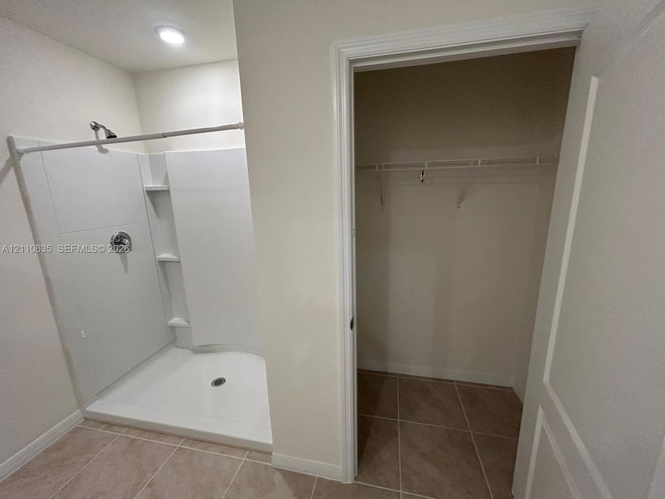 Walk-in shower with a white acrylic surround and built-in shelving, complemented by tile flooring and an integrated closet with wire shelving