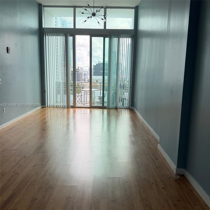 Floor-to-ceiling glass sliding doors with vertical blinds, wood-finish flooring, high ceilings with transom windows, and a multi-arm sputnik-style chandelier