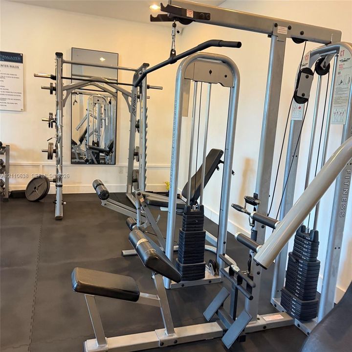 Fitness center featuring rubberized flooring, a wall-mounted mirror, and industrial-grade weight training equipment