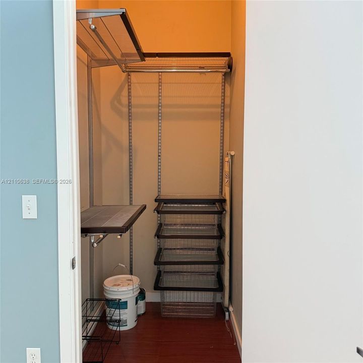 Storage closet featuring an adjustable metal wire shelving system, integrated hanging rod, and stackable sliding wire drawers with wood-finish flooring