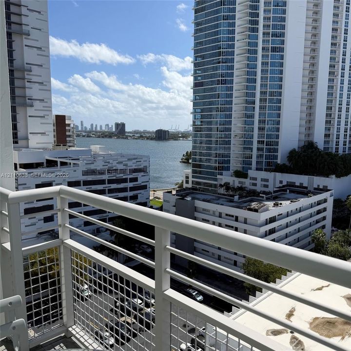 Private balcony with white metal railings and a wire mesh safety enclosure, featuring water and cityscape scenery