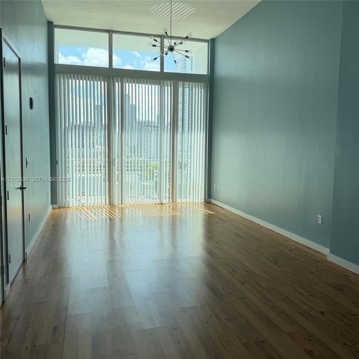 Expansive room featuring floor-to-ceiling windows with transom panels, wood-finish flooring, and a modern multi-arm sputnik chandelier