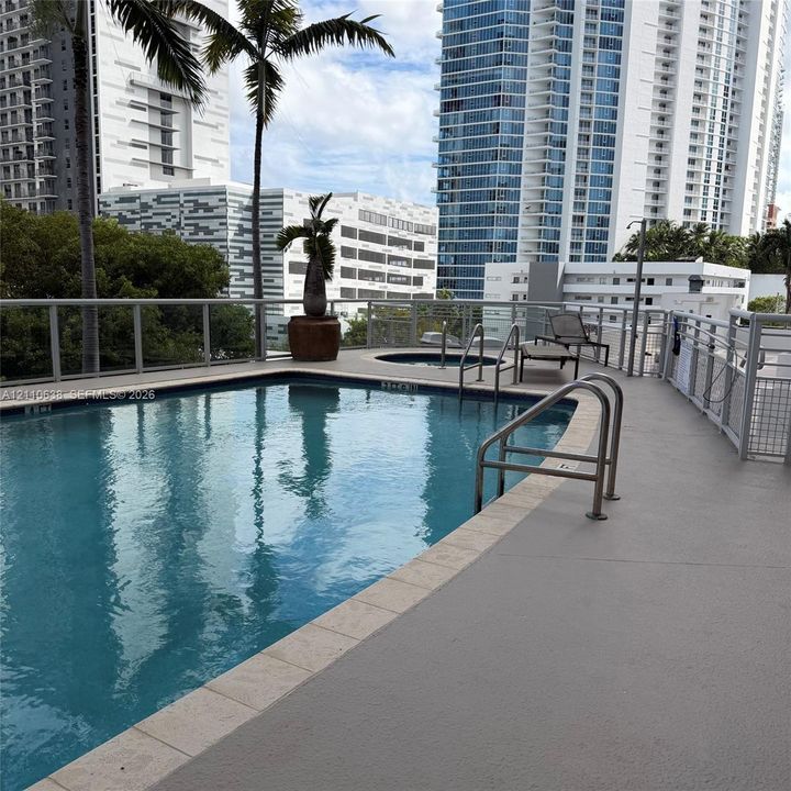 Outdoor swimming pool with integrated spa and metal handrail entry, featuring a surround deck and metal railing enclosure