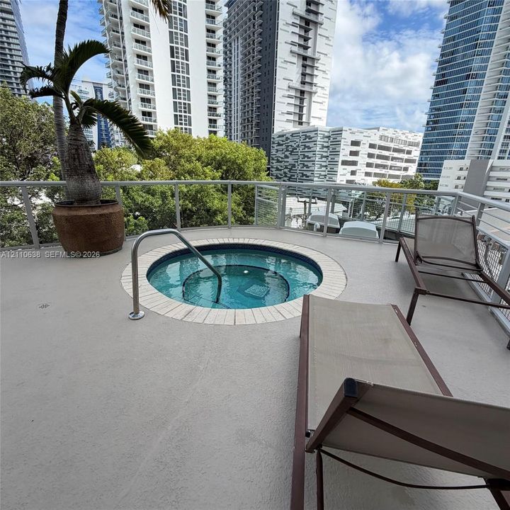 Elevated terrace featuring an in-ground jetted spa, light-toned textured flooring, and a glass-paneled railing