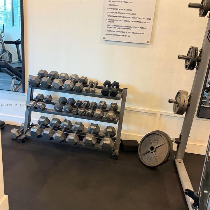 Fitness facility featuring a tiered metal dumbbell rack and a structural weight machine with black rubberized flooring