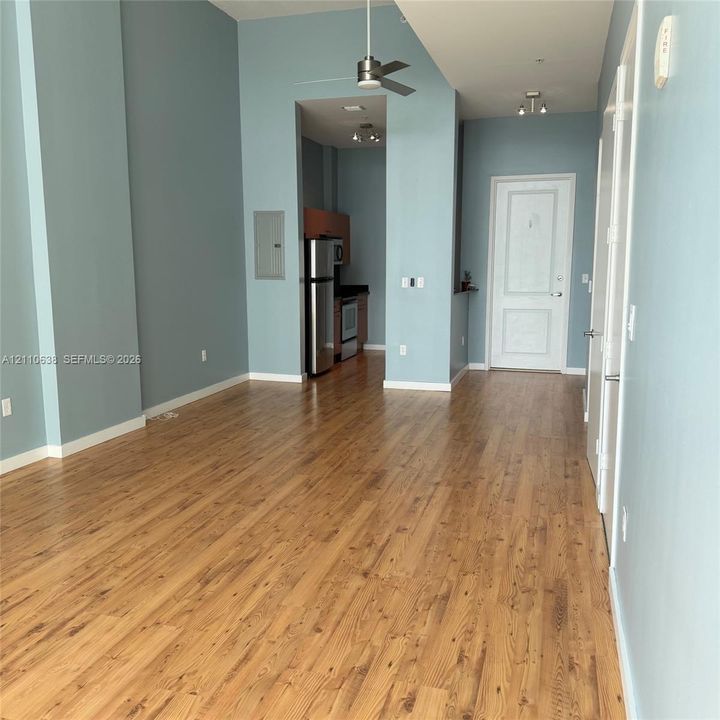 High-ceilinged interior space featuring wood-finish flooring, recessed lighting, a brushed-metal ceiling fan, and stainless steel kitchen appliances