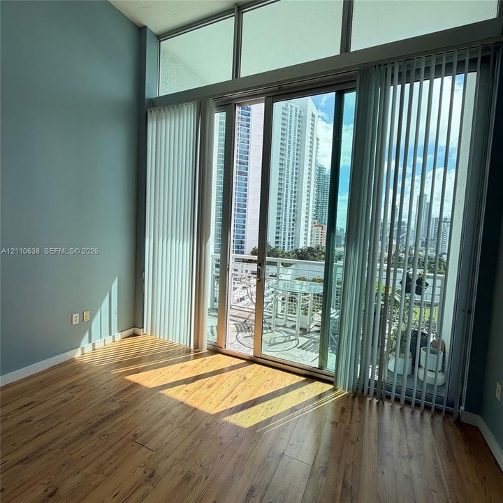 Floor-to-ceiling glass sliding doors with overhead clerestory windows, wood-finish flooring, and an integrated balcony featuring a metal railing