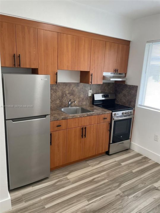 Kitchen featuring flat-panel wood-finish cabinetry, stainless steel appliances, laminate countertops, a stainless steel sink with a pull-down faucet, and wood-finish flooring