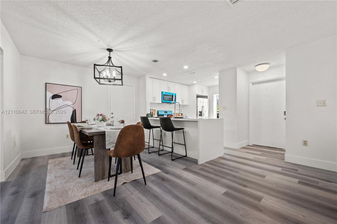 Kitchen featuring white cabinetry, an island with stone-surface countertop, and wood-finish flooring throughout the space, accented by a geometric metal chandelier