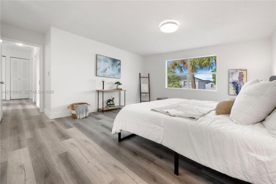 Neutral-toned wood-finish flooring, crisp white walls, dual-panel closet doors, and large single-hung window featuring outdoor palm tree greenery
