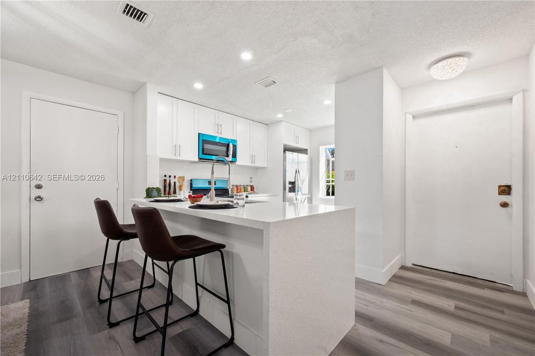 Kitchen featuring white cabinetry, stone-surface breakfast bar with waterfall edge, wood-finish flooring, and stainless steel appliances