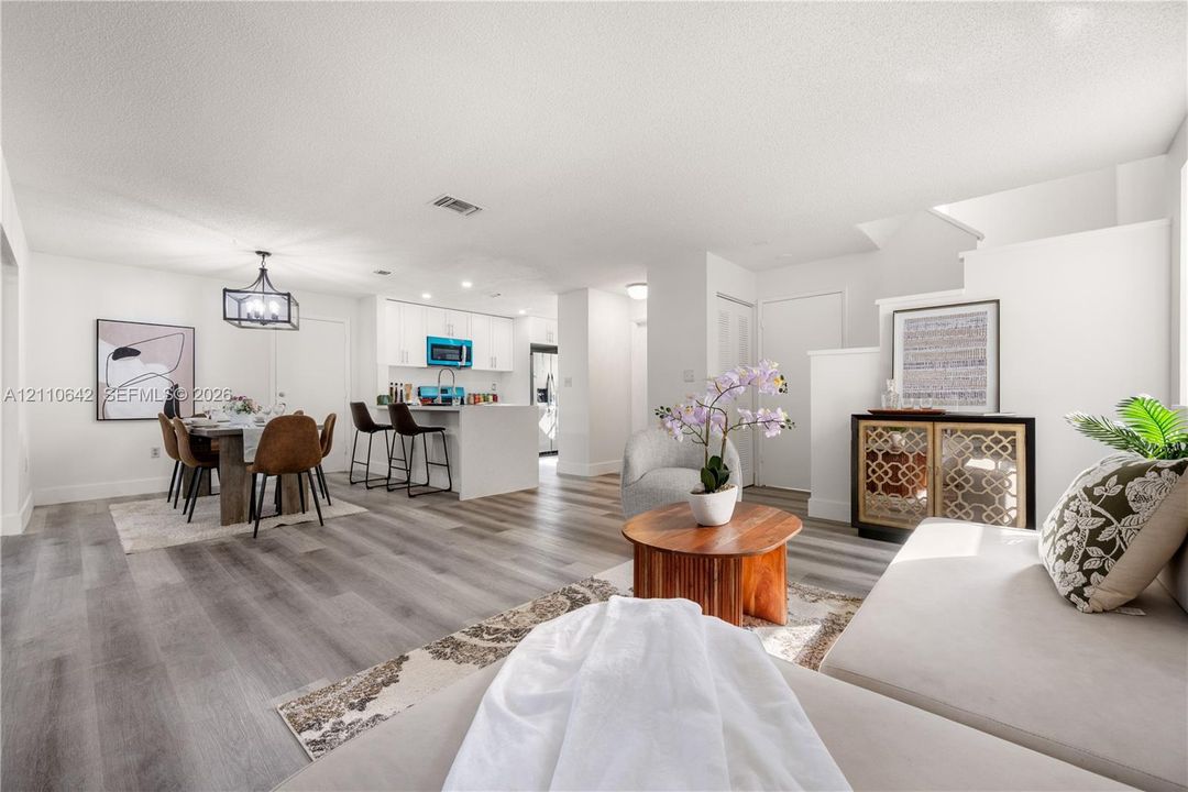Open-concept interior featuring wood-finish flooring, white cabinetry, a kitchen island with stone-surface countertop, and a contemporary geometric hanging light fixture