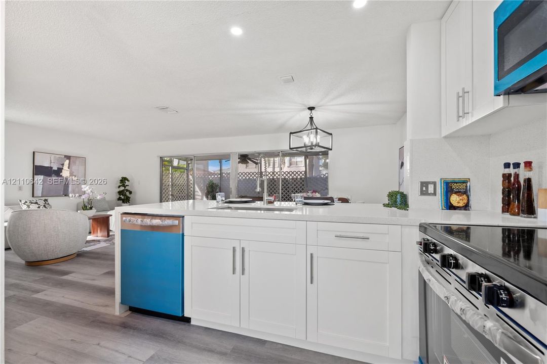 Kitchen featuring white cabinetry, quartz countertops, a stainless steel undermount sink, and wood-finish flooring