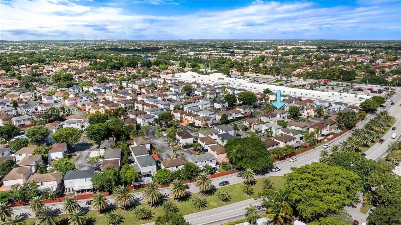 Aerial perspective of a suburban neighborhood featuring residential housing, mature tree canopy coverage, expansive green spaces, and proximity to major thoroughfares