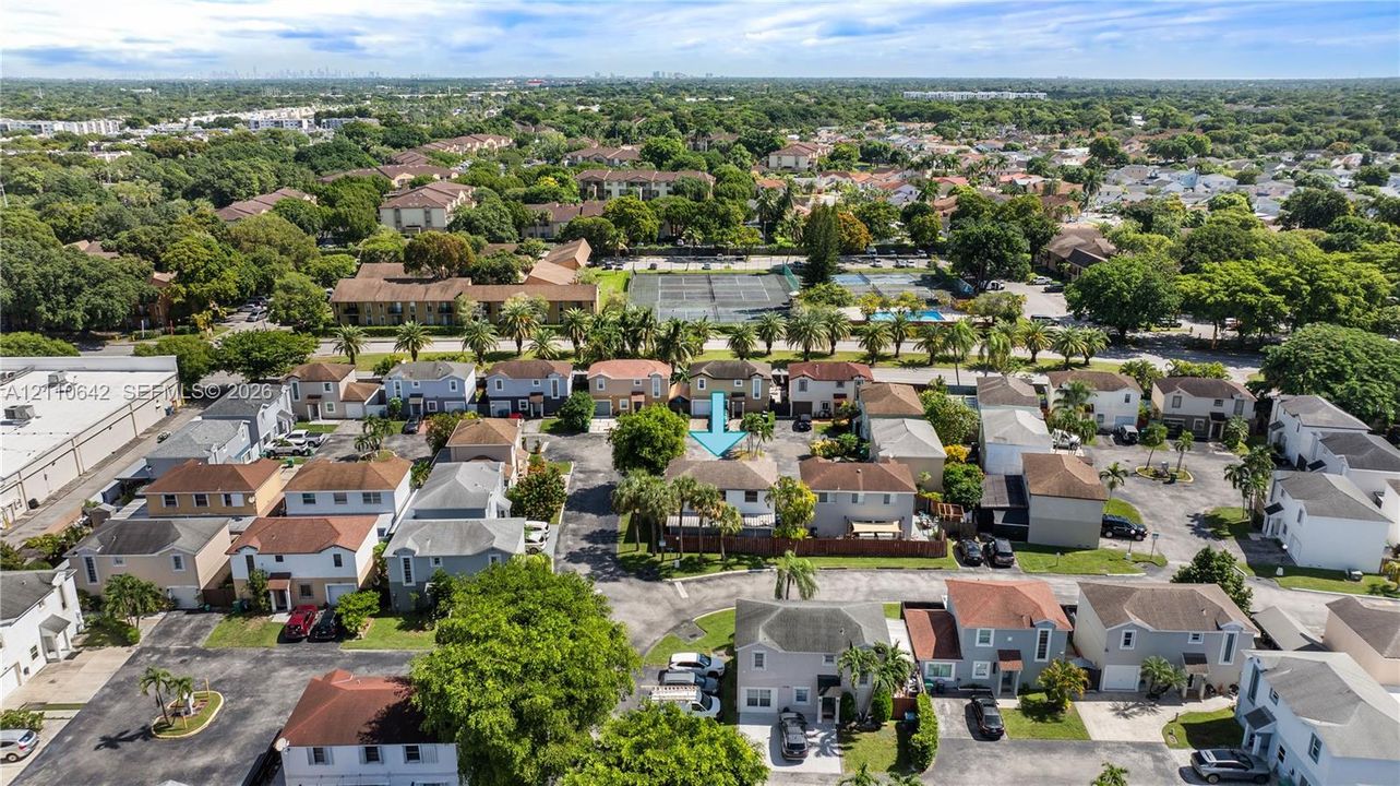 Aerial perspective of a multi-unit residential property featuring a pitched roofline, paved driveway, and established surrounding greenery