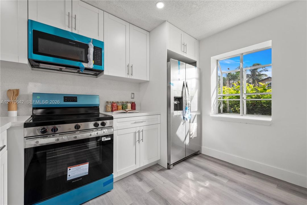 Kitchen featuring white shaker-style cabinetry, wood-finish flooring, stainless steel side-by-side refrigerator, slide-in range with glass cooktop, and an over-the-range microwave