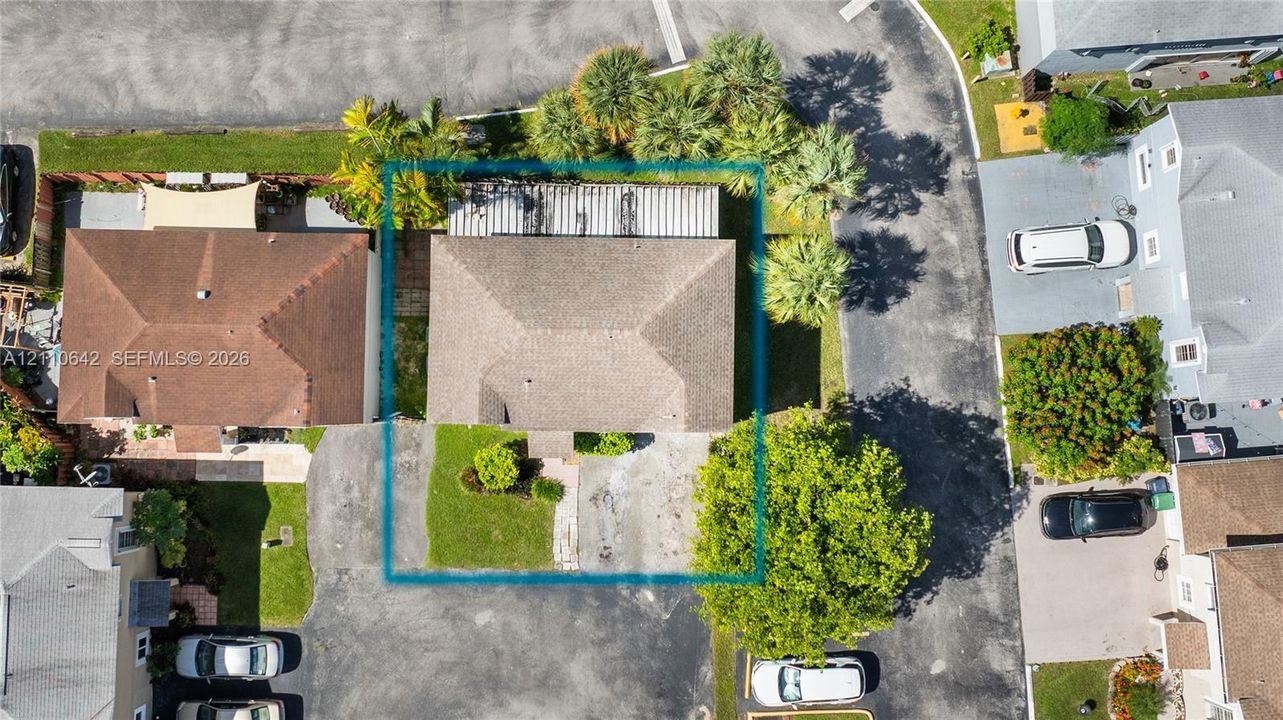 Aerial perspective featuring a hip-roof structure, concrete driveway, and landscaped front lawn with mature palms