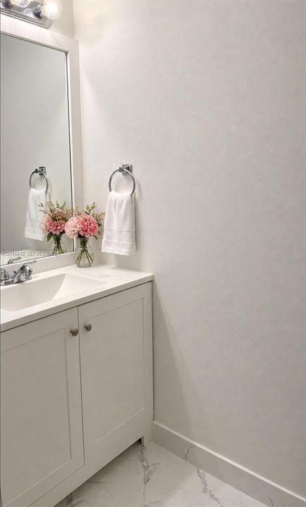 White vanity cabinet with a stone-composite countertop, integrated rectangular sink, chrome-finished faucet, framed mirror, and polished stone-finish floor tile