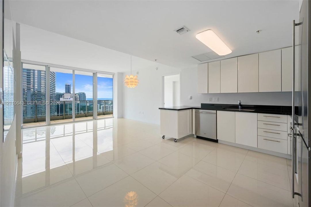 Open-concept kitchen featuring white flat-panel cabinetry, contrasting dark countertops, stainless steel appliances, polished tile flooring, and floor-to-ceiling glass panel doors
