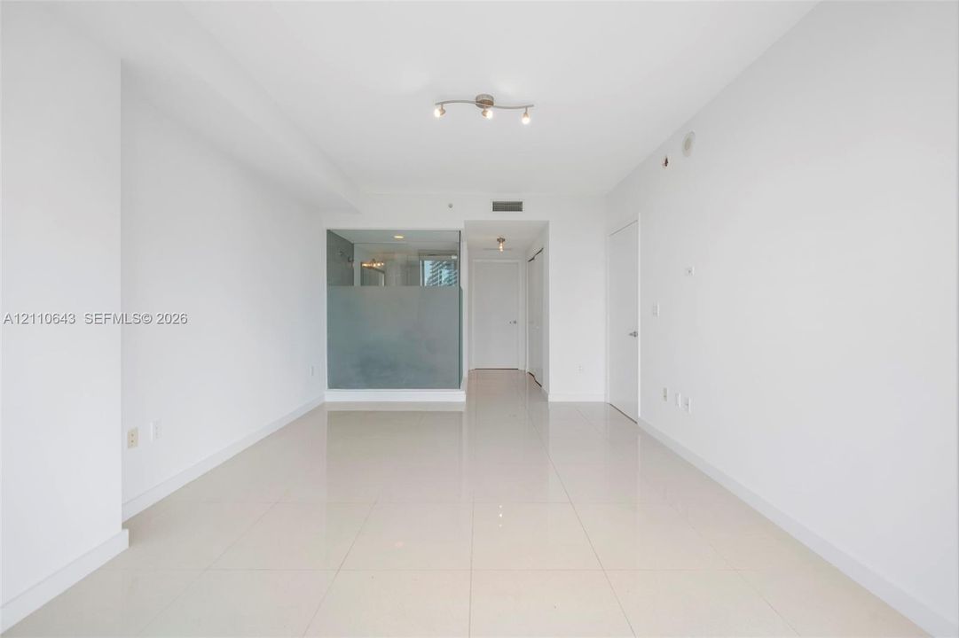 Open-concept interior featuring large-format ceramic tile flooring, neutral wall finishes, semi-opaque glass partition, and adjustable track lighting