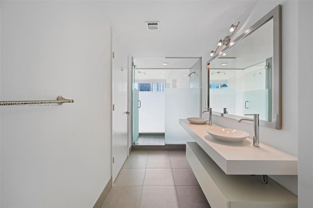 Floating vanity featuring a dual-sink countertop, vessel sinks with tall gooseneck faucets, large wall-mounted mirror, and tile flooring